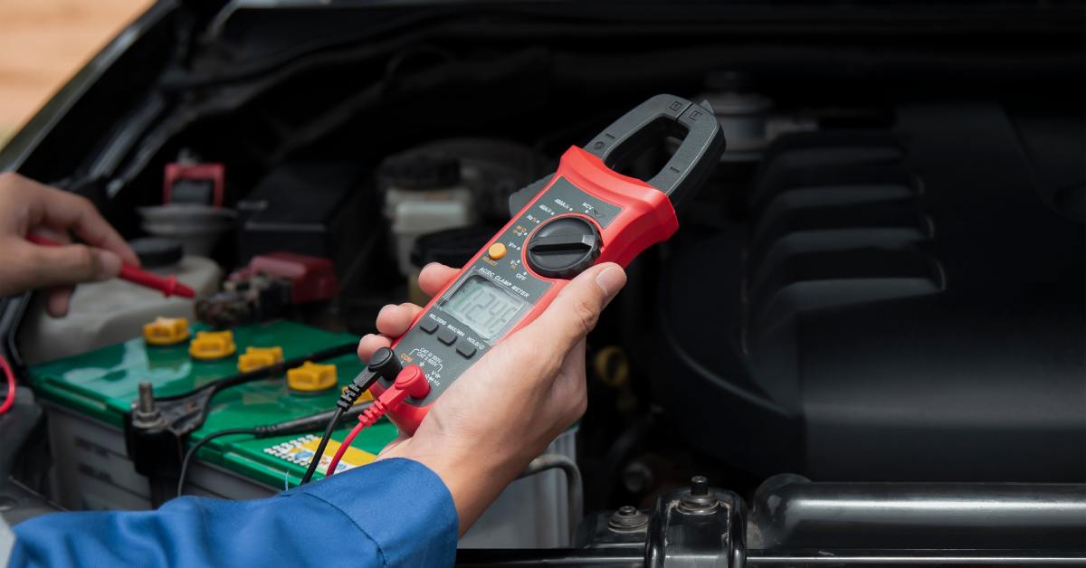 Close-up of an auto repair mechanic’s hand using a special diagnostic tool to check the battery inside a car.