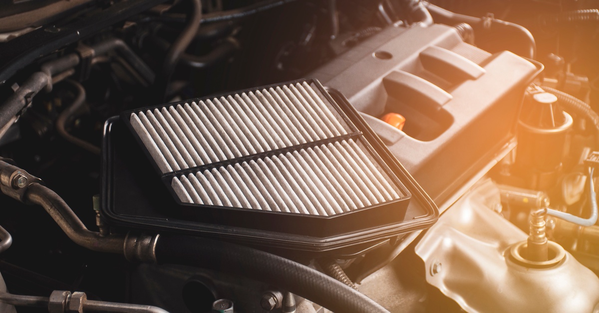 A dirty automotive air filter sits on the top of the interior car components with the hood popped up.