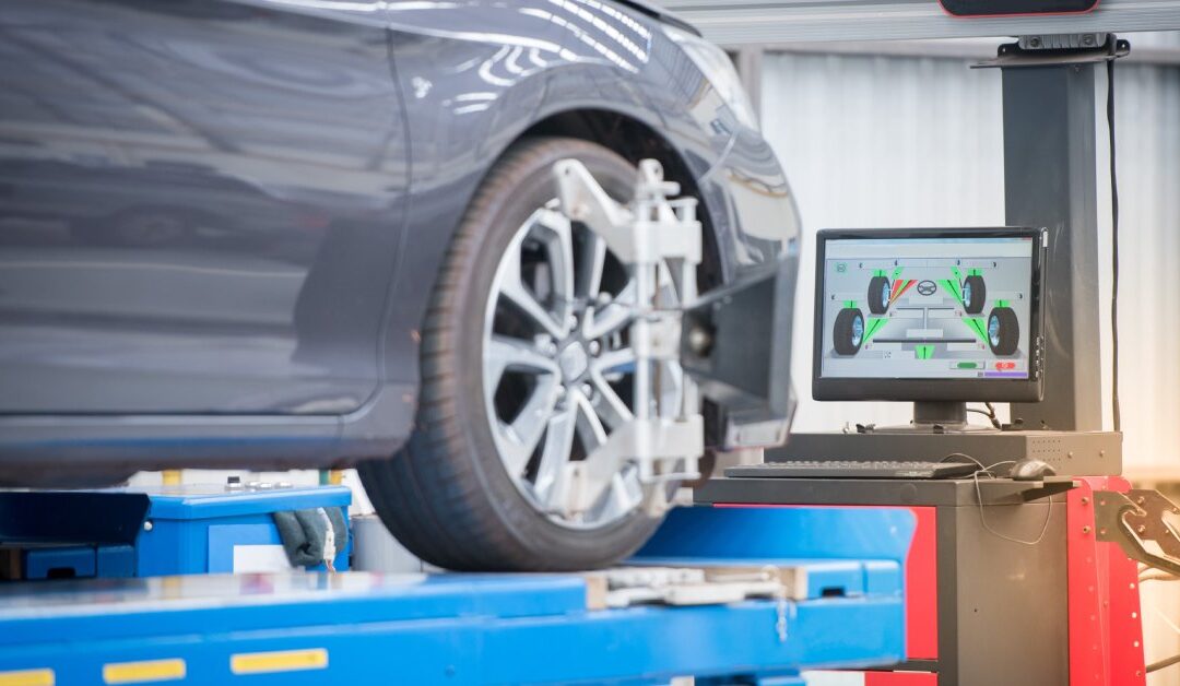 A gray car on a blue garage lift getting the front passenger tire worked on. The computer screen shows all four tires.