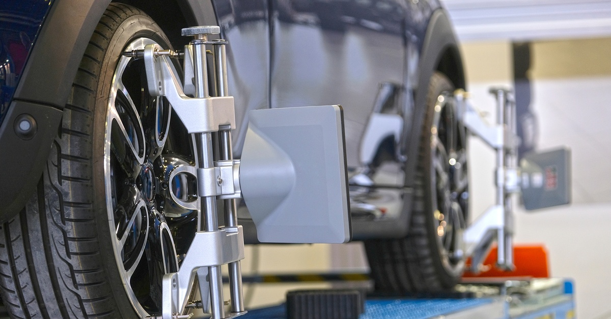 A close-up of a vehicle on an auto lift receiving a wheel alignment on the rear and front tires. The car is navy blue.

