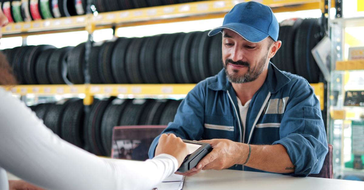 A mechanic at the customer service desk of the car repair shop receiving a payment from the customer.