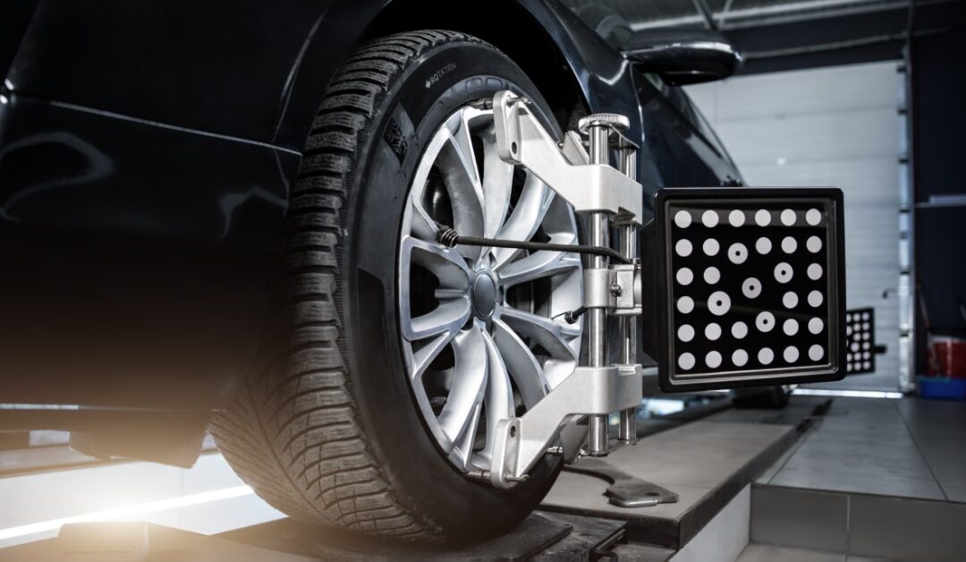 A close-up of a vehicle on a car lift at the repair shop. There is a device hooked to the tire for an alignment service.