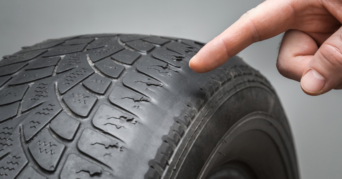 A close-up of a mechanic pointing to a tire. The tire is showing visible signs of worn tread and damage.